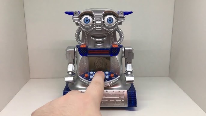 A photo of someone pointing at an IR-V. It’s made of gray plastic with a screen in the centre, resembles both ET and older robot toys, and has human eyes for some reason?